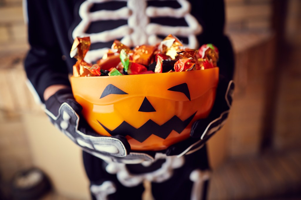 A child in a costume holding a bowl of Halloween candy